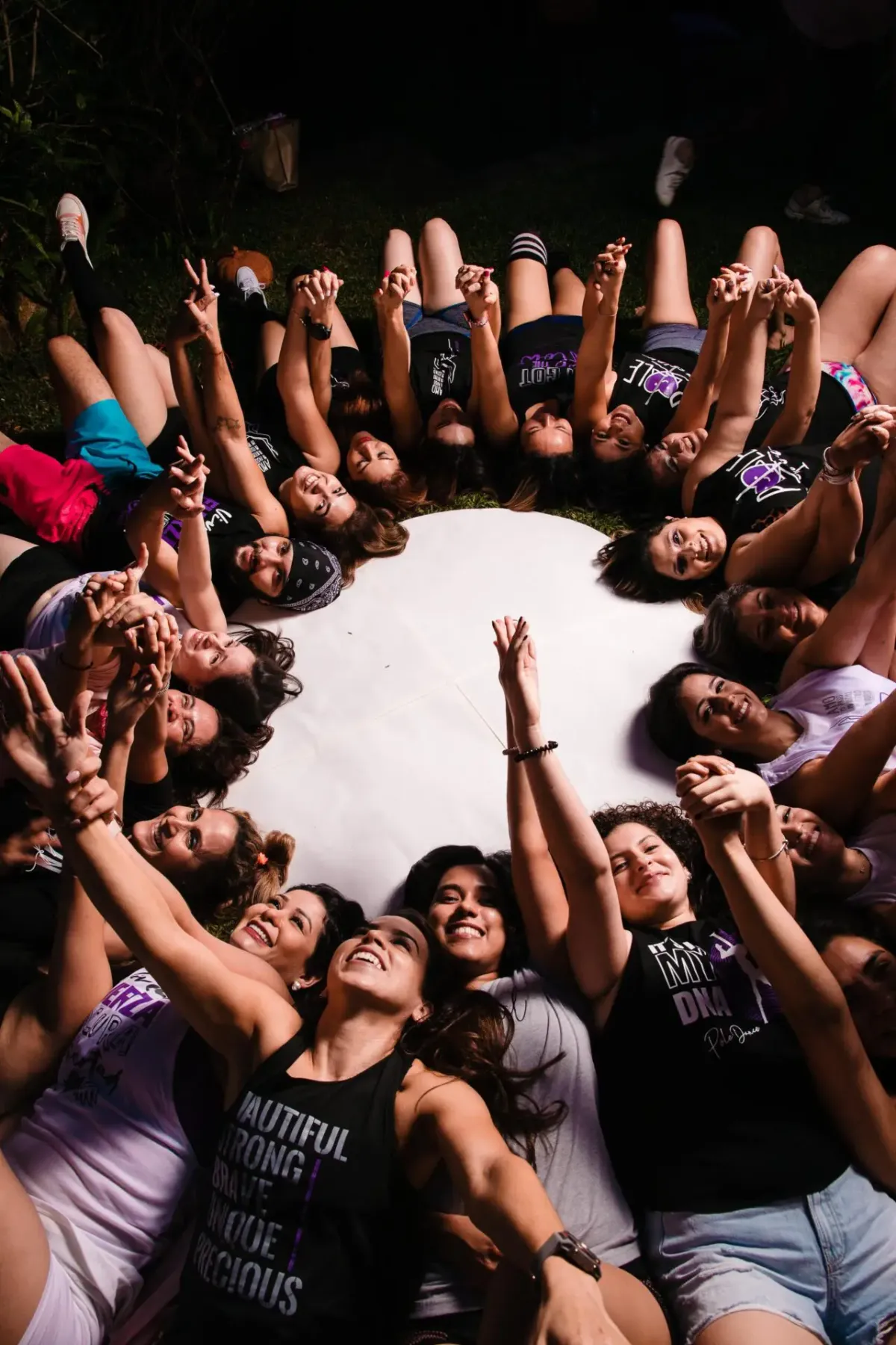 Comunidad de mujeres tumbadas en círculo con las manos hacia el centro, vistas desde arriba
