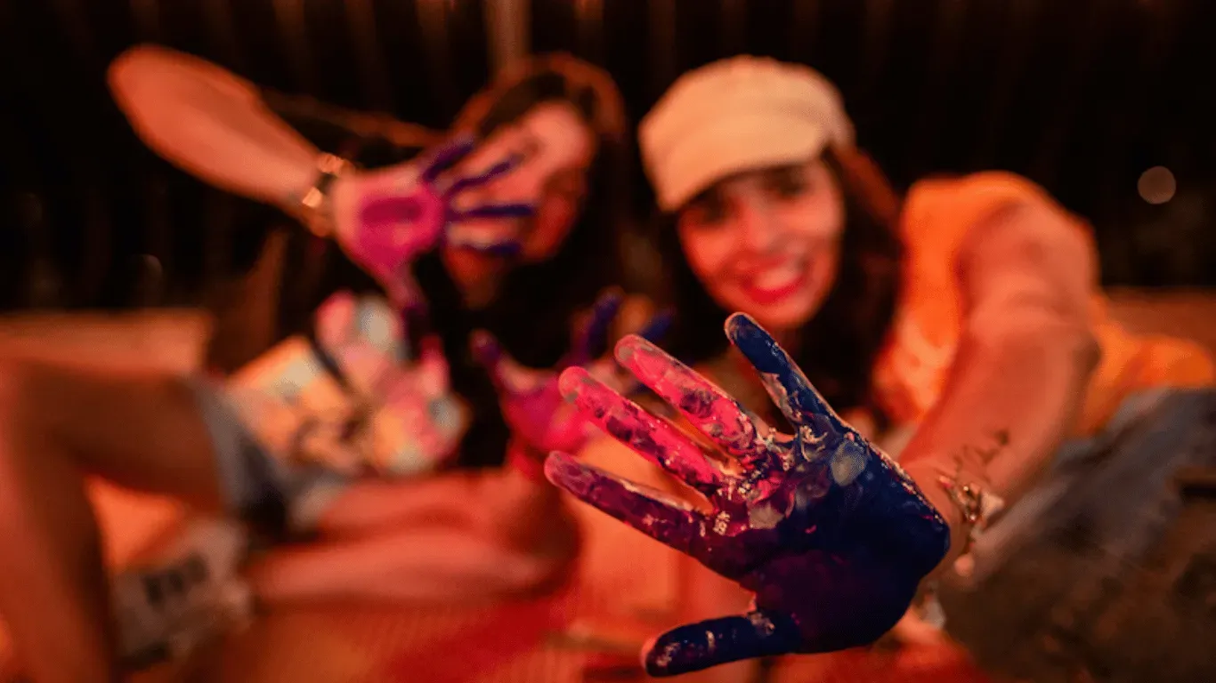 Mujeres muestran a cámara sus manos pintadas de colores, luz cálida
